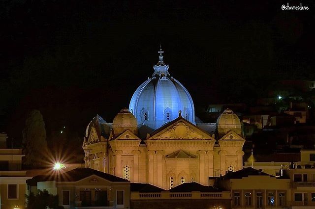 A brightly lit church with a blue dome stands against a dark sky in an urban setting.