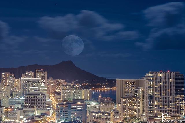 Cityscape of Honolulu at night with Diamond Head in background and full moon.