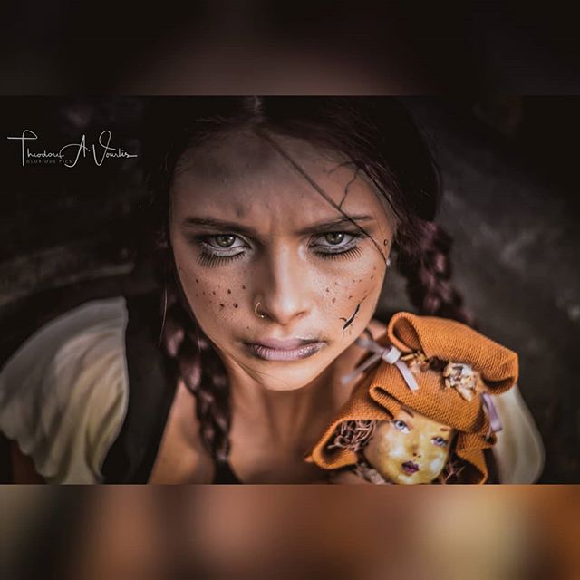 A woman with dark makeup and braids holds a doll, creating a mysterious and moody image.