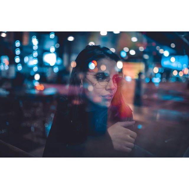 A woman with glasses gazes thoughtfully in a blurred city night setting, perfect for editorial or social media use.