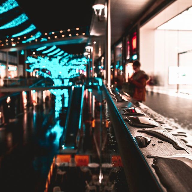 A person stands inside a brightly lit shopping mall, captured with a shallow depth of field.