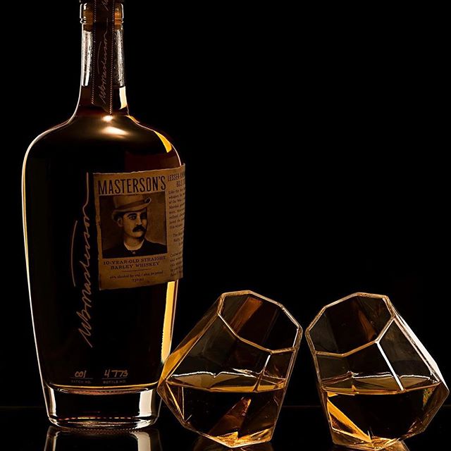 An elegant whiskey bottle and two diamond-faceted glasses filled with amber liquor create a sophisticated bar scene.