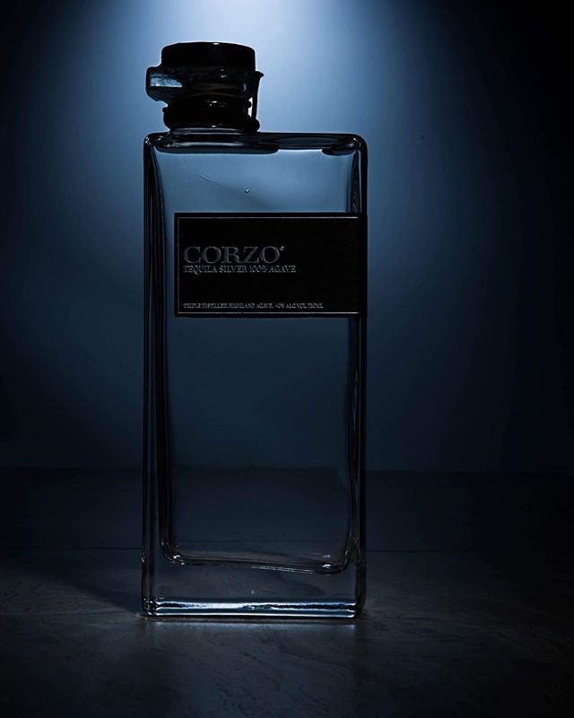 A bottle of Corzo tequila stands illuminated in a studio setting, perfect for advertising and social media content.
