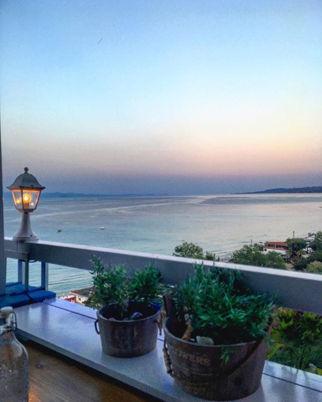 A serene ocean view from a balcony with potted plants during a colorful sunset.