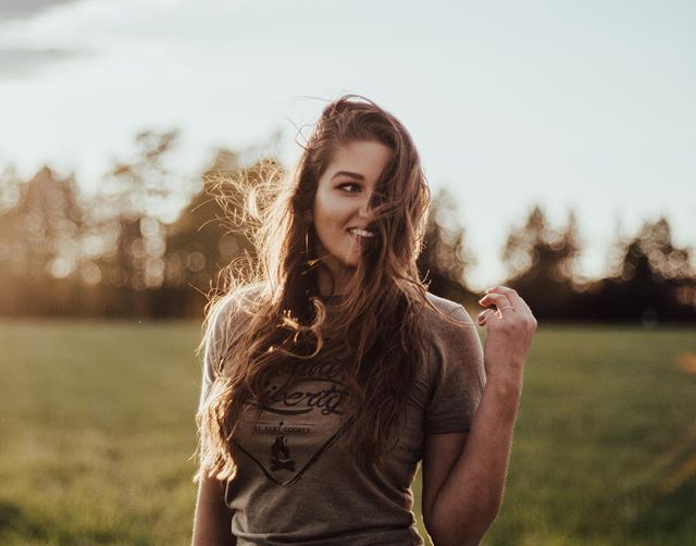 A happy woman smiles in a field, bathed in golden sunlight. Natural, candid shot.