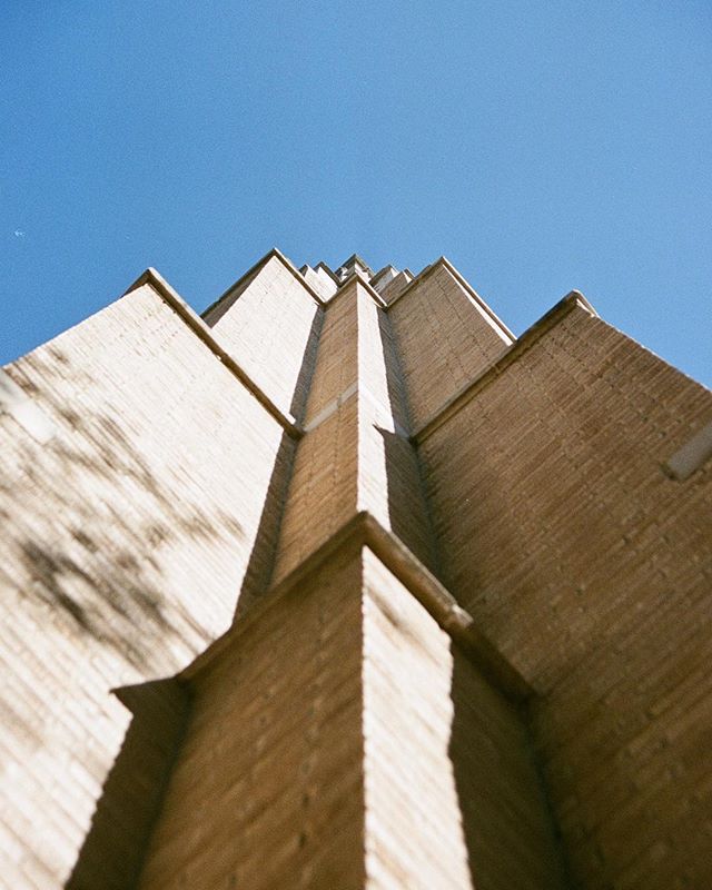 A worm's eye view captures the geometric details of a beige brick building against a clear blue sky.