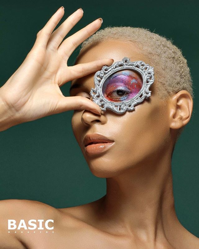A striking portrait of a woman with creative eye makeup, framed by a decorative hand-held mirror.