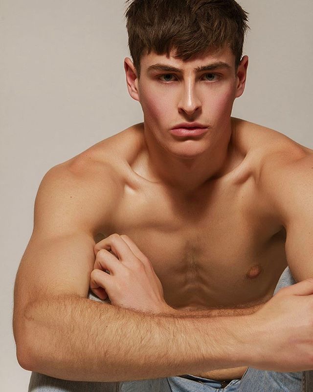 A muscular man poses shirtless in a studio with soft lighting for a health and fitness campaign.