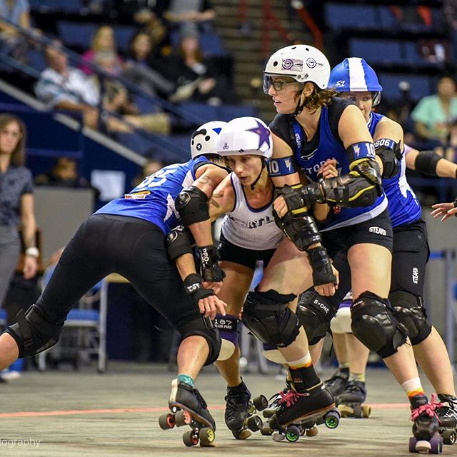 Four female roller derby athletes compete in an intense match at an indoor arena, showcasing strength and determination.