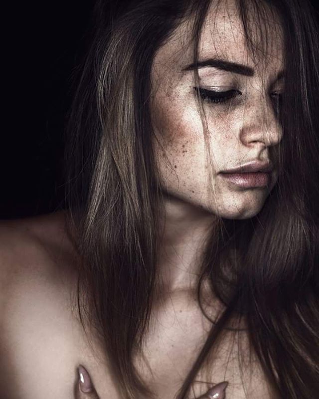 A sensual portrait of a brunette woman with freckles against a dark background.