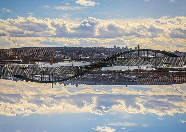 An abstract reflection of a bridge and cityscape under a cloudy sky creates a serene and modern urban scene.