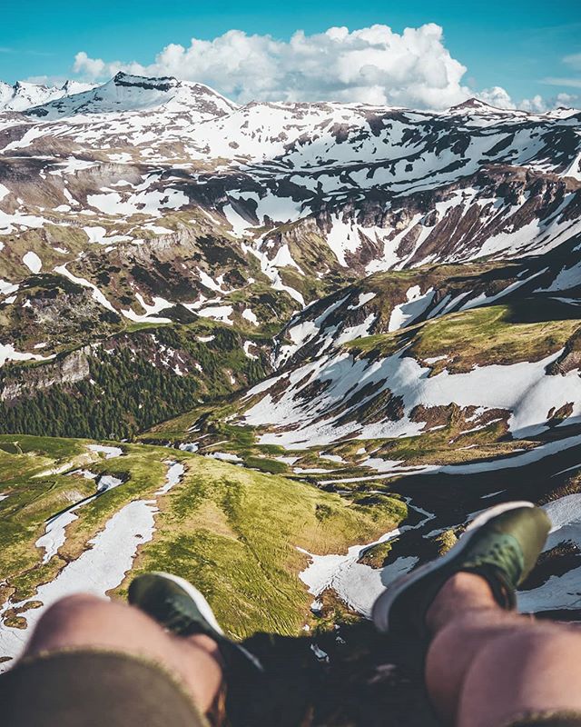 A scenic mountain landscape view with snow-capped peaks and green valleys, seen from a high vantage point.