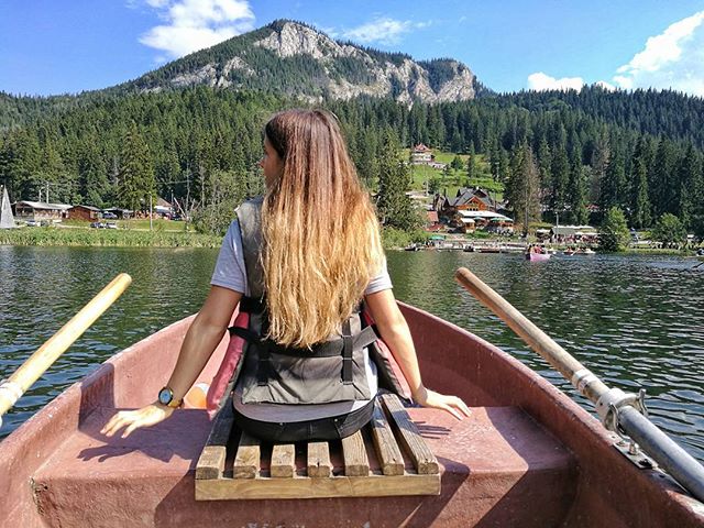 Woman paddles a rowboat on a calm lake with a mountain backdrop on a sunny day.