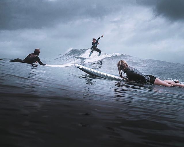 Three surfers enjoy the waves on a cloudy day, creating a dynamic and sporty scene.