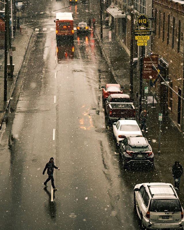 A snowy city street featuring cars and pedestrians on a wet, reflective road during a winter day.