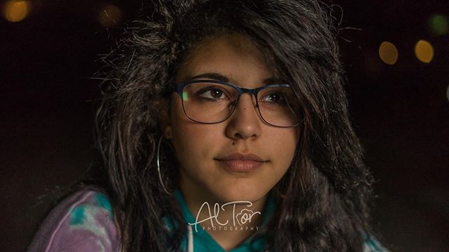 Portrait of a young woman with glasses looking off into the distance with a blurred background.
