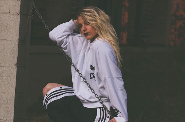 A woman in a white sweatshirt and black shorts poses outdoors with a chain.