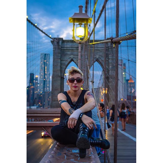 A stylish woman sits on Brooklyn Bridge with the city skyline in the background, capturing an urban lifestyle moment.
