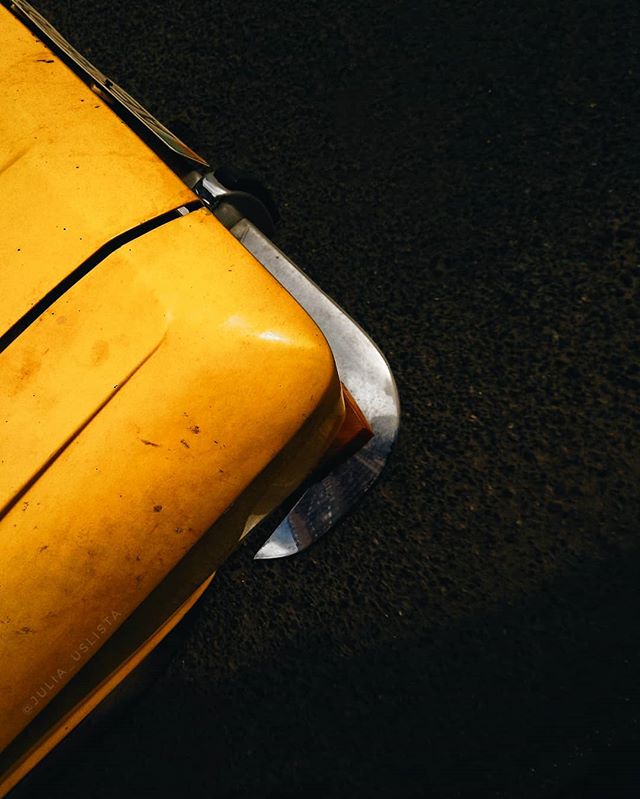A close-up captures the yellow bumper and chrome of a vintage car parked on a dark asphalt surface.
