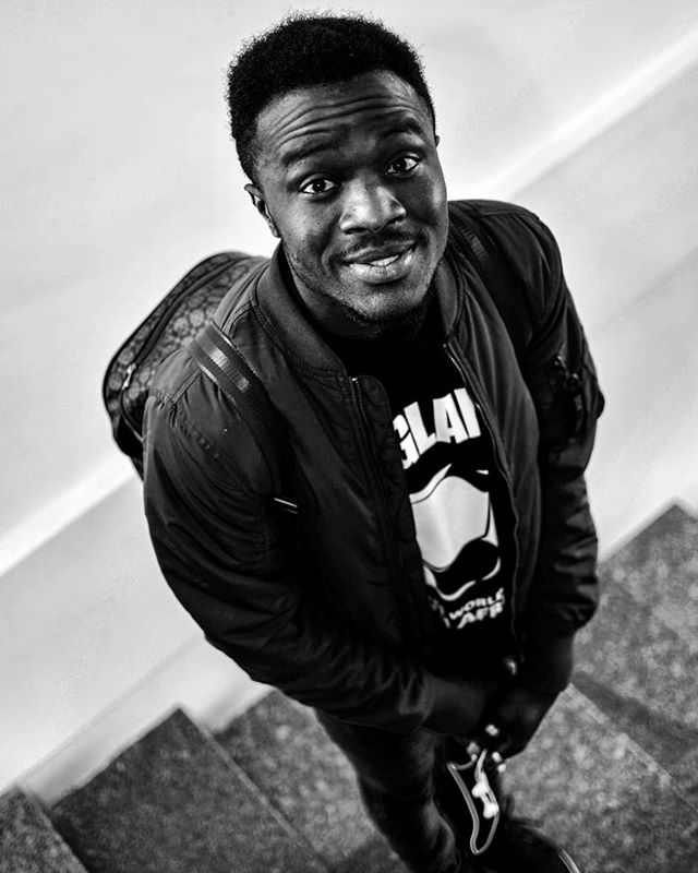 A stylish black man in a jacket and backpack is captured in a striking low-angle shot on a staircase.