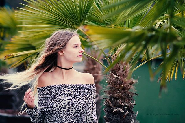 A woman in an off-shoulder top stands in front of palm trees, enjoying the tropical breeze and serene atmosphere.