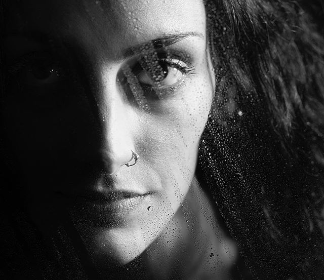 A black and white portrait of a woman with water droplets on her face creates an emotional, dreamy image.