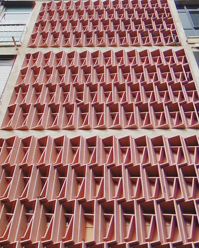 Modern building facade featuring a geometric brise soleil design with a warm, earthy color palette and soft lighting.