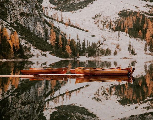 Tranquil boats on Lake Braies in the Italian Alps, surrounded by colorful autumn trees and majestic mountains. A perfect scenic escape.