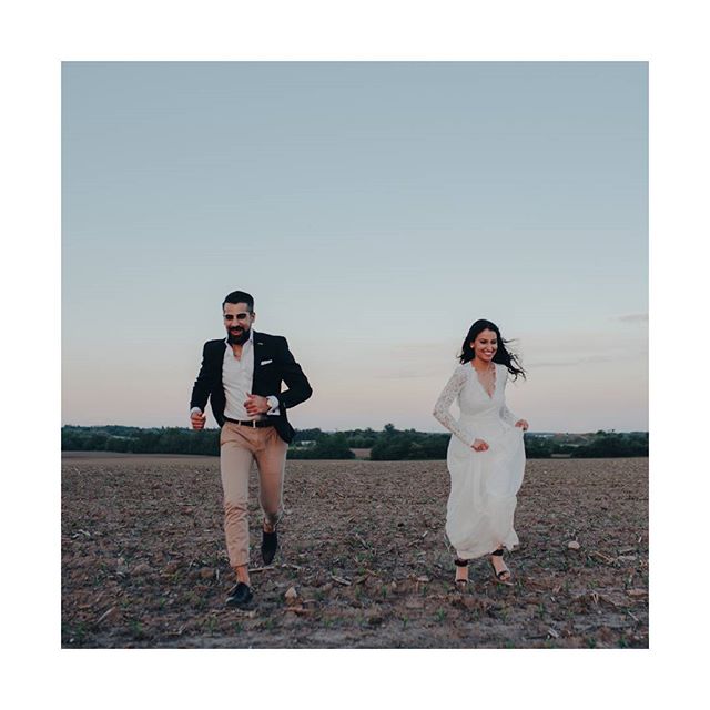 A bride and groom run happily through a field, celebrating their wedding day.