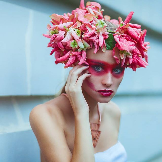 A woman wears a pink flower crown and striking makeup in a dreamy, sensual portrait.