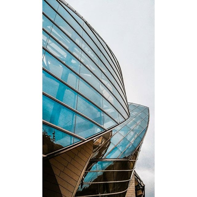 A captivating architectural facade showcases modern design with reflective glass, creating a sleek, abstract form against a neutral sky.