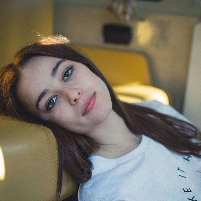 A serene young woman relaxes inside a van, bathed in soft natural light.