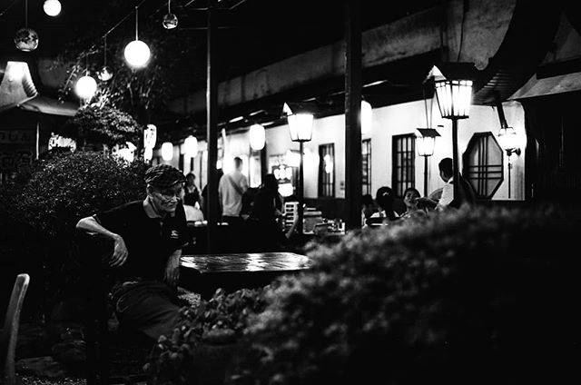 A black and white image shows people at an outdoor restaurant at night, lit by lanterns.