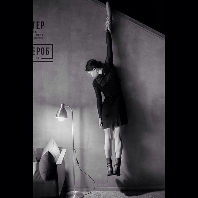 A woman in a dress and boots is holding onto the edge of the ceiling in a black and white photo.