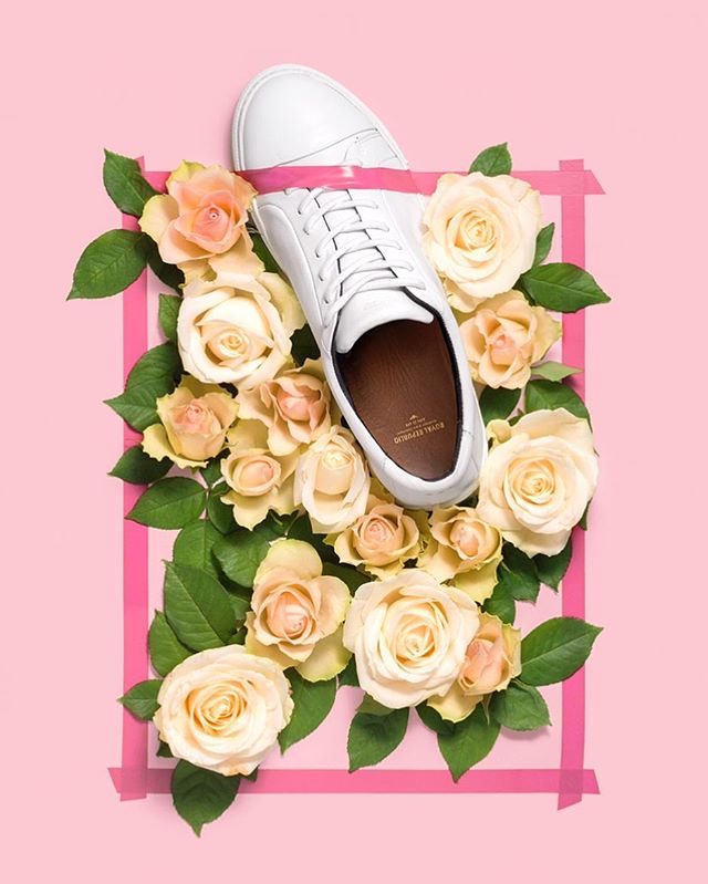 White sneakers surrounded by peach roses and framed with pink tape on a soft pink background. 