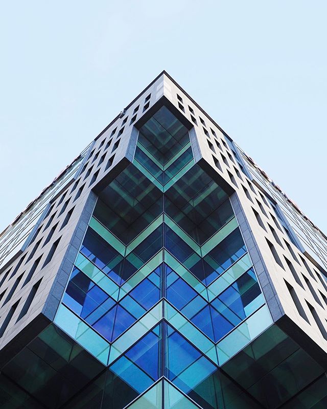A modern building with a geometric glass facade is shot from a low angle, showcasing architectural design and urban development.