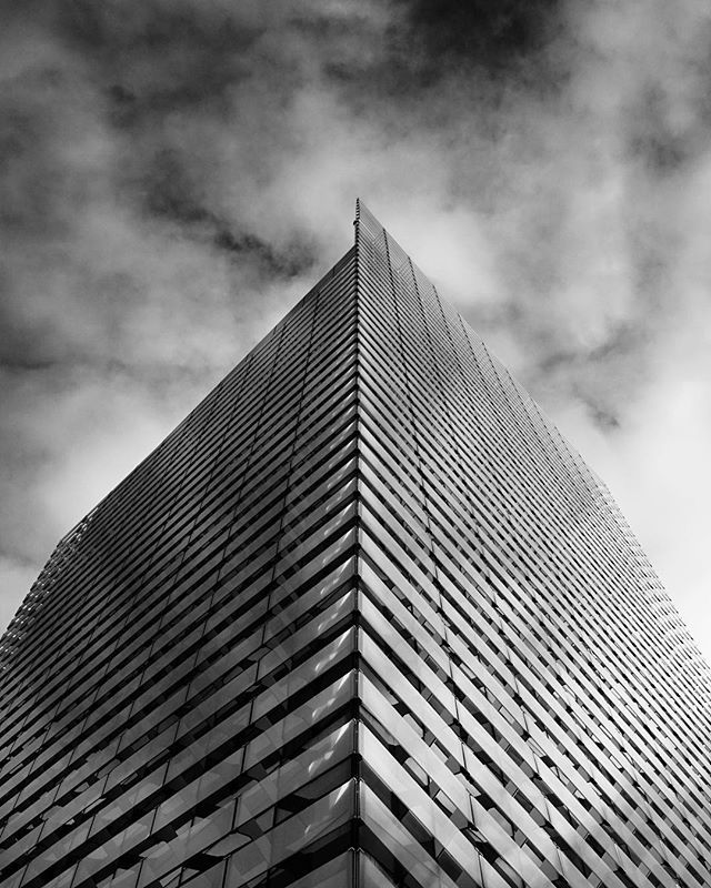 A modern skyscraper rises against a dramatic sky, captured in striking black and white.