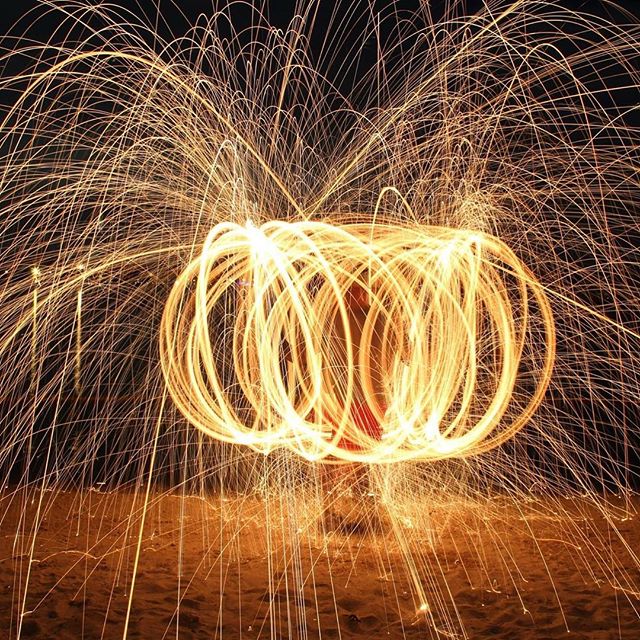 Abstract light painting on a beach at night, showcasing swirling patterns and trails of sparks.