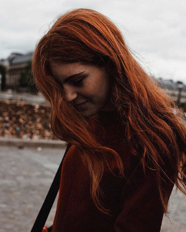A redhead woman poses outdoors in the city.