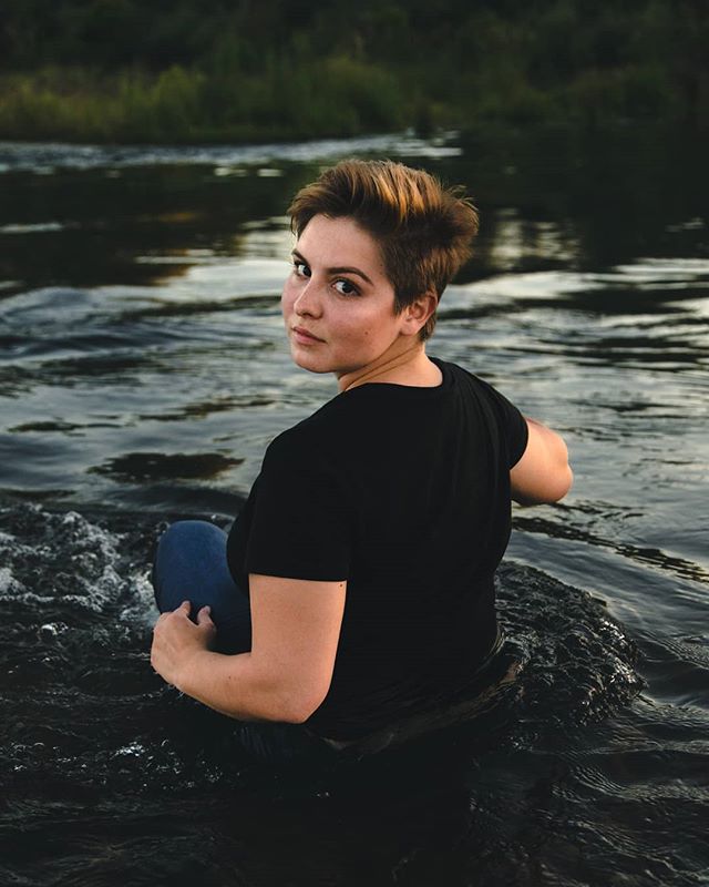 A woman sits in a river, looking back over her shoulder.