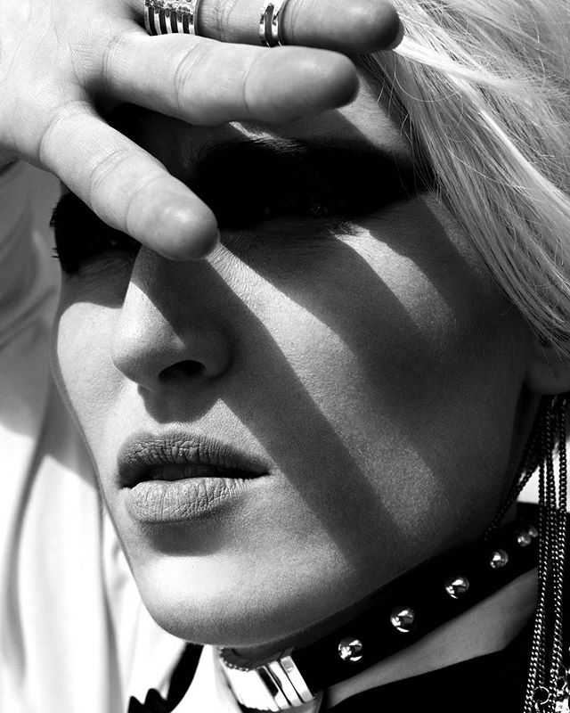 A striking black and white portrait of a woman with bold makeup, shielding her eyes with a hand adorned with rings.