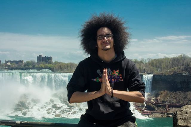 Man with afro poses in front of a waterfall, creating a serene travel moment.