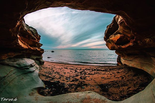A scenic view from a cave entrance overlooking the ocean and beach with a beautiful sky.