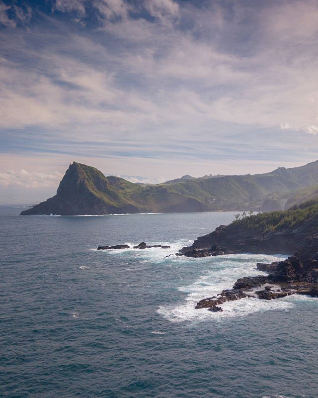 Scenic view of an island coastline with lush green mountains meeting the blue ocean under a partly cloudy sky.