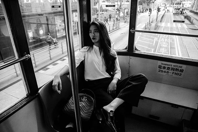 A stylish woman sits in a tram, gazing out the window at the city in this black and white image.