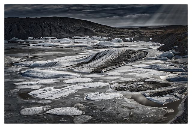 A monochrome landscape showing icebergs in a glacial lagoon against a dramatic sky in Iceland.