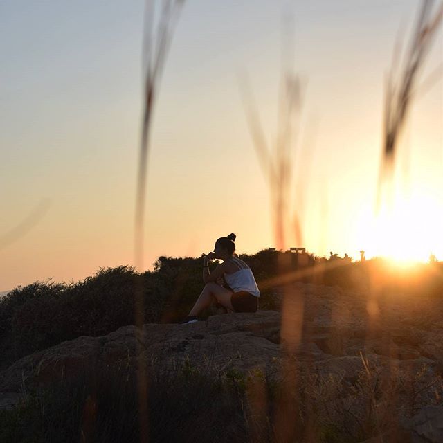 Woman sits on a hilltop enjoying a serene sunset, lost in thought. Ideal for wellness and mindfulness themes.