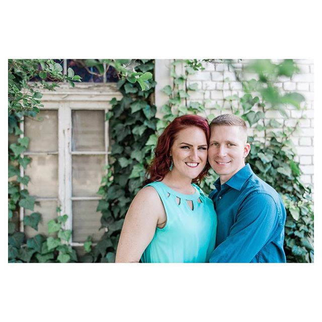 A happy couple poses in front of a brick wall covered in ivy, creating a natural, intimate portrait.