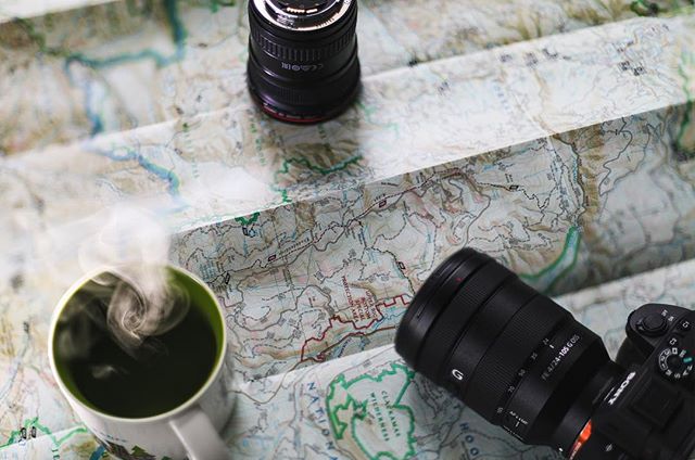 Camera gear and a steaming cup of coffee rest on a detailed map, ready for adventure planning.