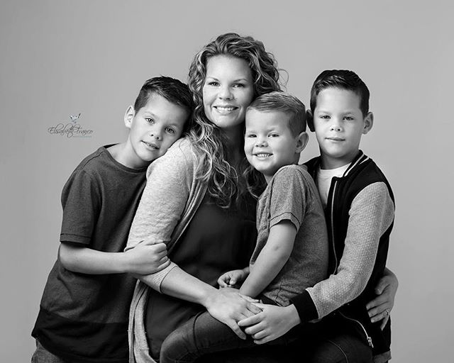 A mother poses with her three sons in a black and white family portrait, showcasing a close family bond.